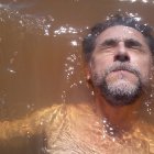 Man with beard in water, bubbles, necklace, yellow shirt, serene expression