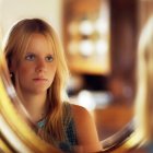 Blonde girl reflected in round mirror with warm lighting
