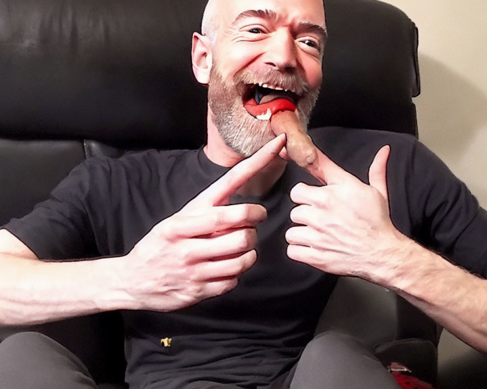 Bald man in black shirt pointing at tongue with spicy snack, laughing
