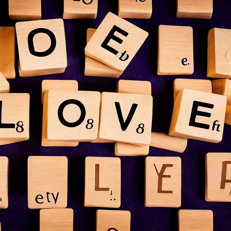 Wooden blocks spell "LOVE" on purple surface with scattered letter and number tiles