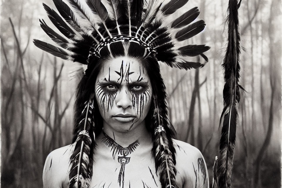Monochrome portrait of person in feathered headdress with face paint, gazing intensely in forest.