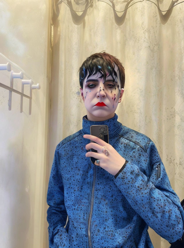 Person with dramatic black and red makeup in mirror selfie wearing blue patterned jacket
