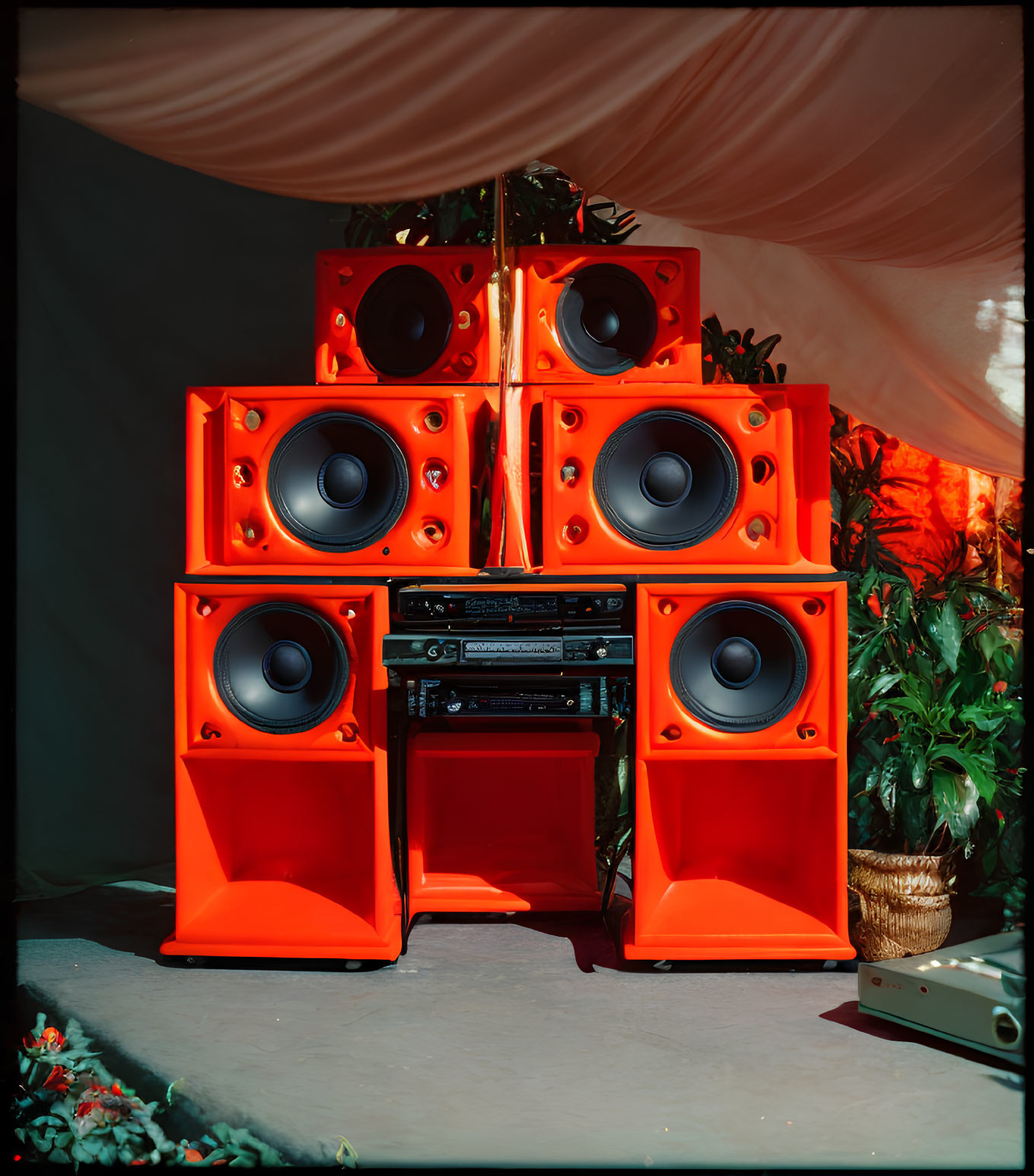 Colorful orange speakers with stereo system and plants on draped background