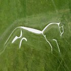 Stylized white horse with flowing mane prancing on grassy hills under green sky