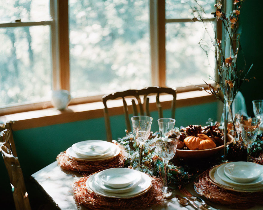 Autumnal table setting with woven placemats, white dishes, glasses, pumpkins, and