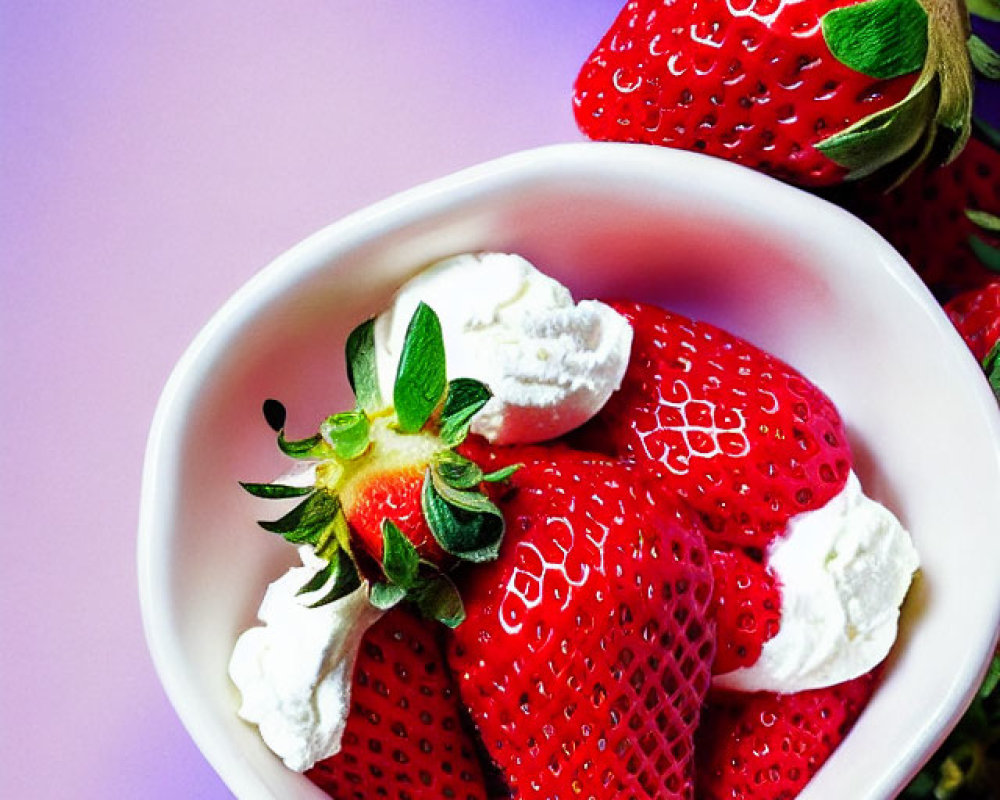 Ripe strawberries and whipped cream in white bowl on purple backdrop