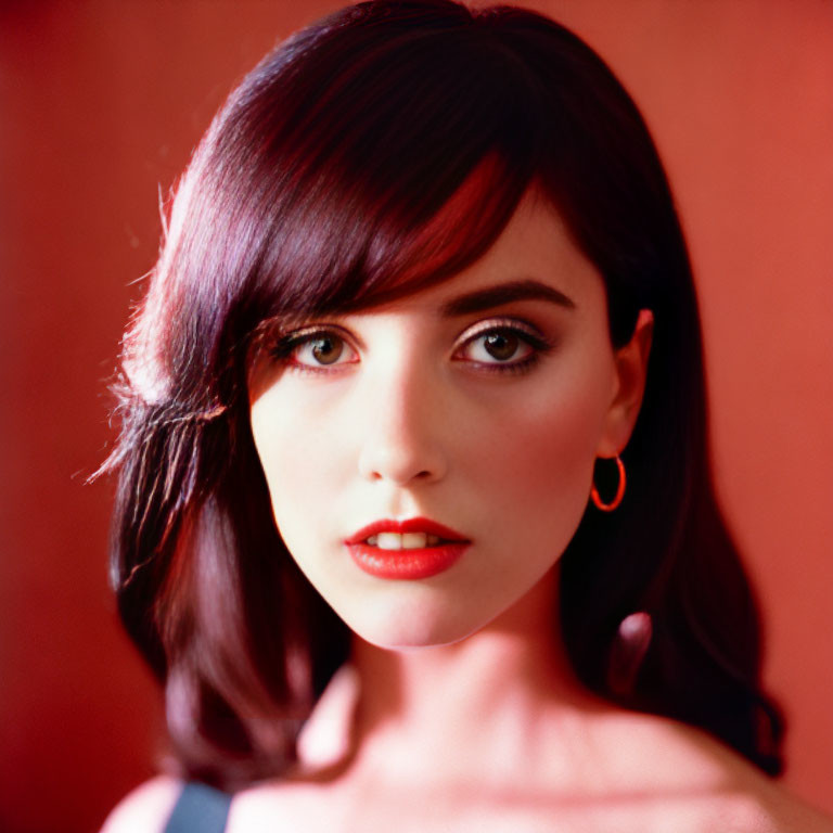 Dark-haired woman with red lipstick and hoop earrings against red backdrop