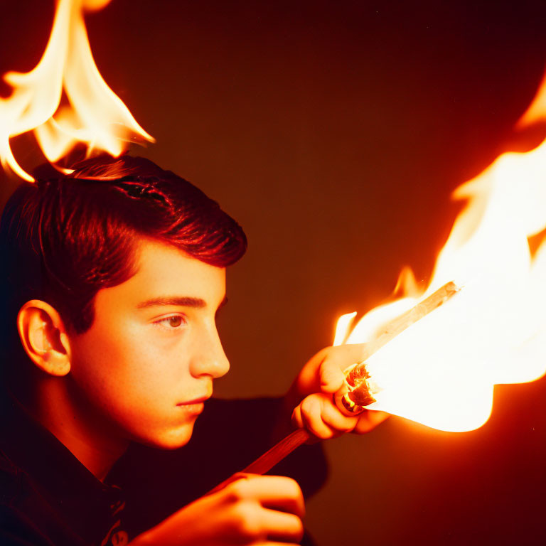 Person holding flaming stick against dark background.
