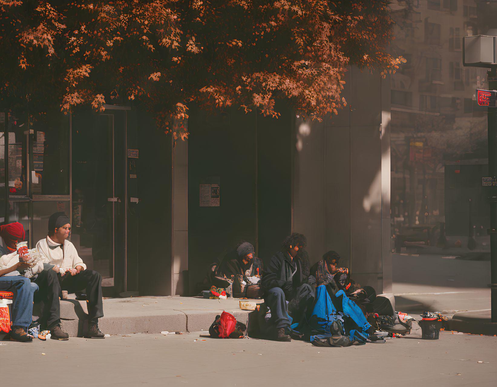 City sidewalk scene with people under autumn trees and scattered belongings