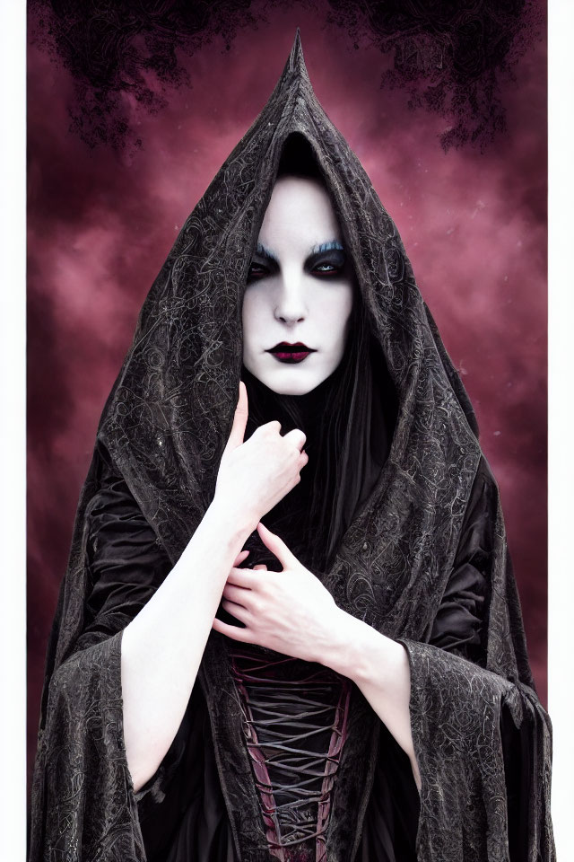Pale-skinned person in dark makeup under hooded black cloak against red and purple sky