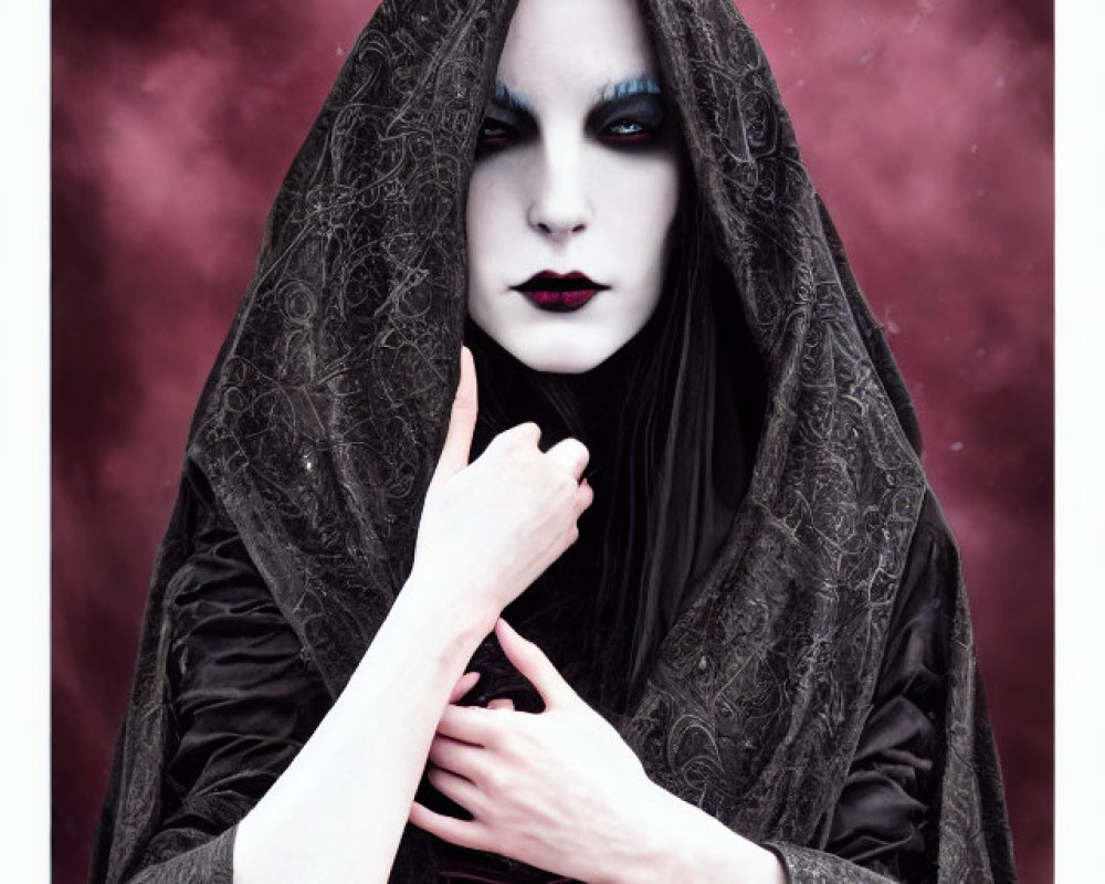 Pale-skinned person in dark makeup under hooded black cloak against red and purple sky