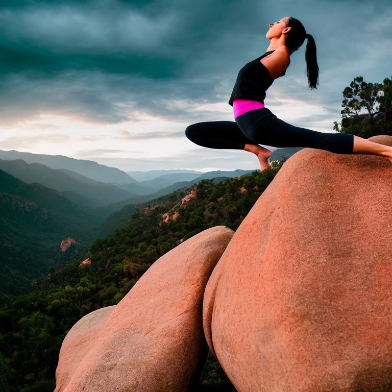 Woman practicing yoga on boulder with dramatic sky and mountains.