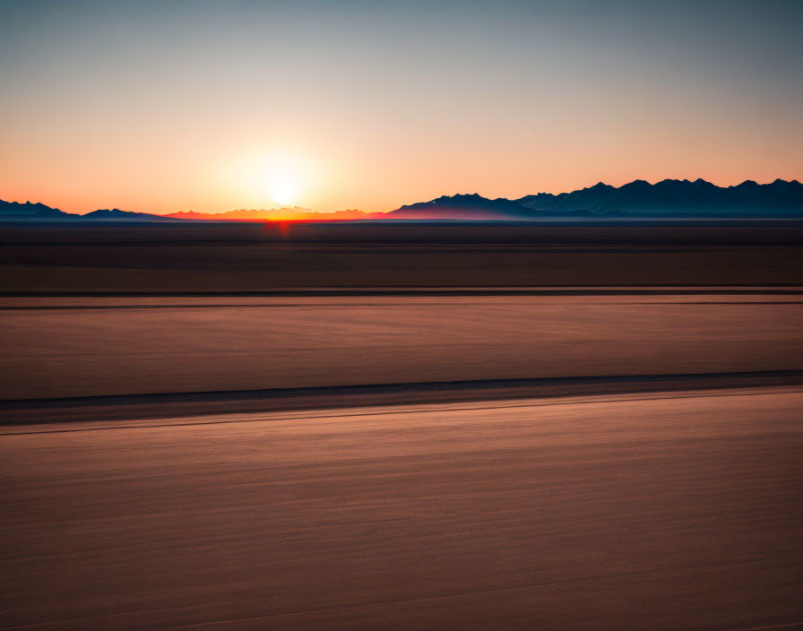 Vibrant desert sunset with silhouetted mountains and smooth sand