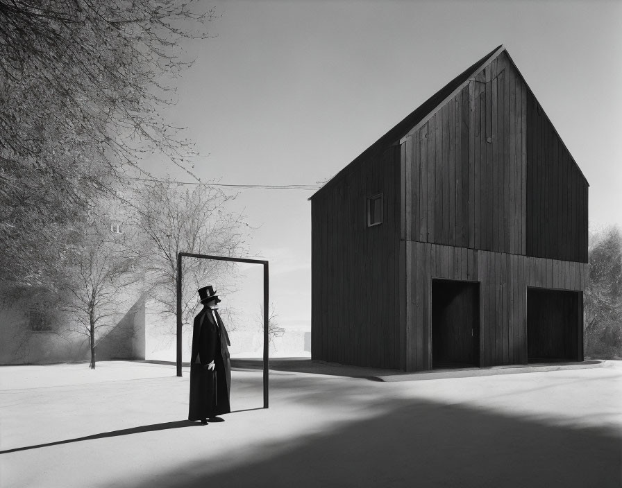 Monochrome image of person in long coat and hat in doorway with dark barn and trees under bright sky