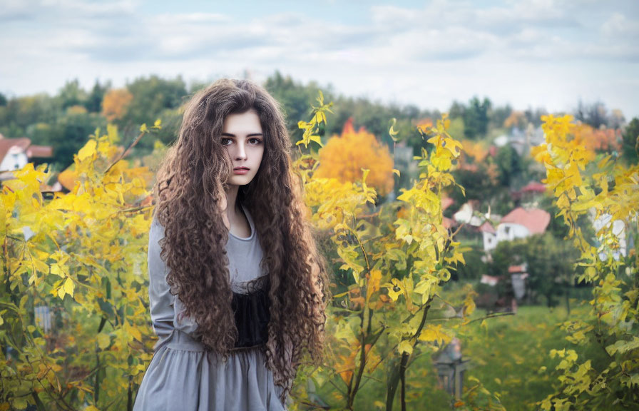 Young woman with curly hair in autumn setting with cloudy sky & houses.