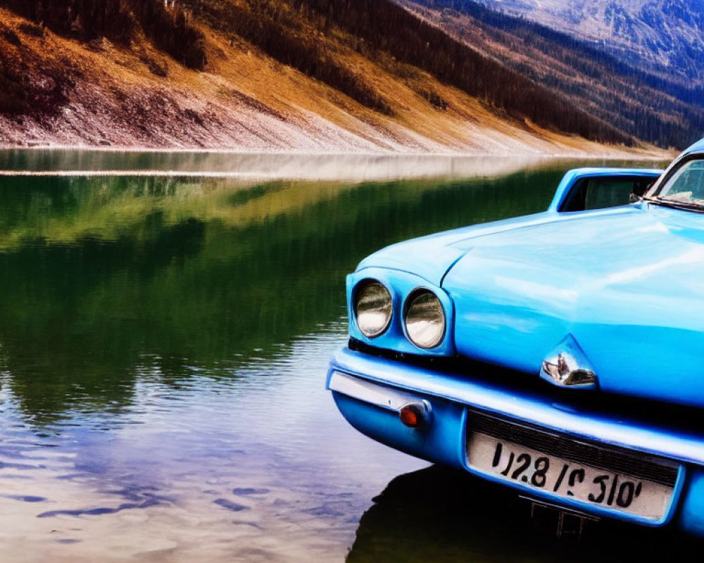 Vintage blue car by serene lake with forested hills & mountains