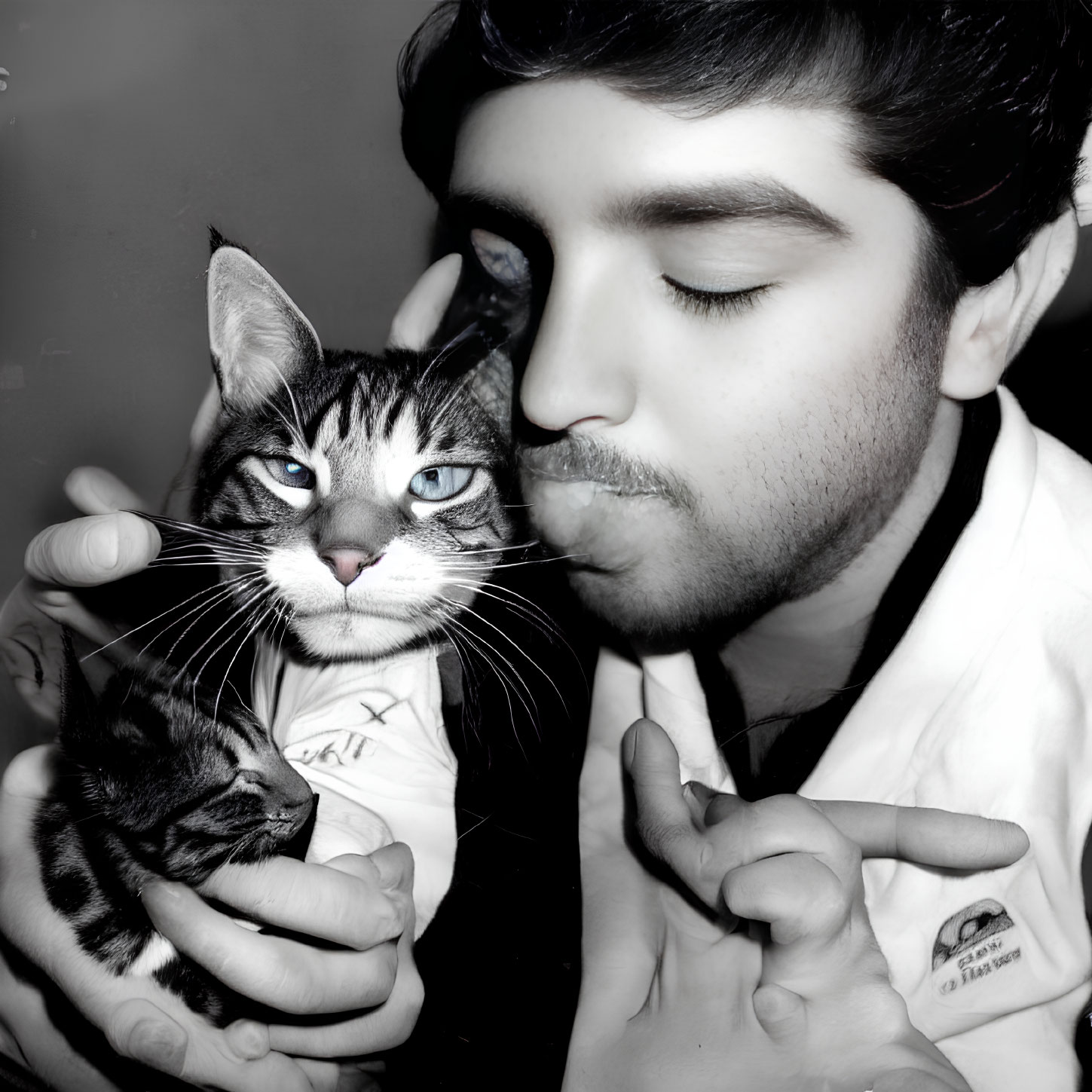 Person affectionately kissing large cat with smaller kitten in hand against grayscale backdrop