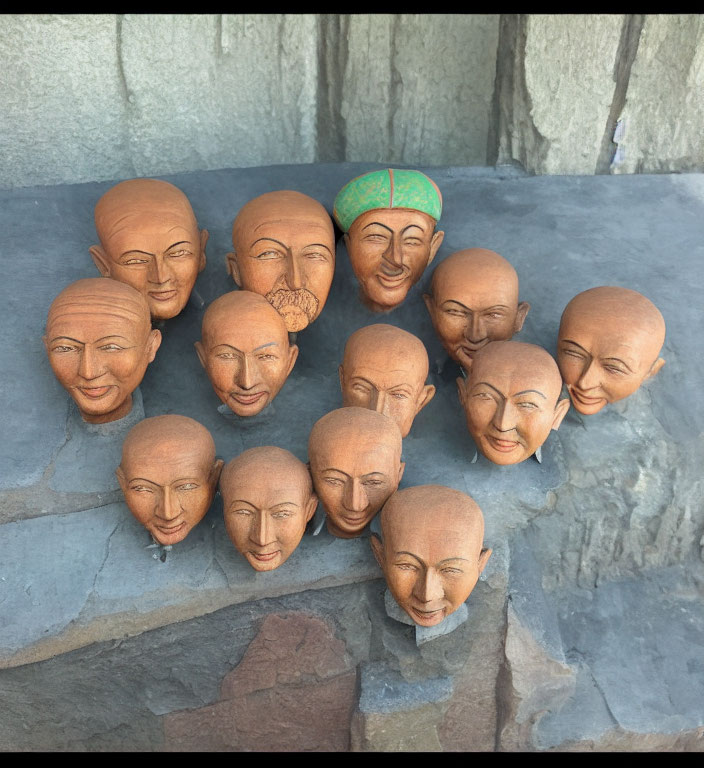Assorted wooden carved heads with different expressions on stone ledge