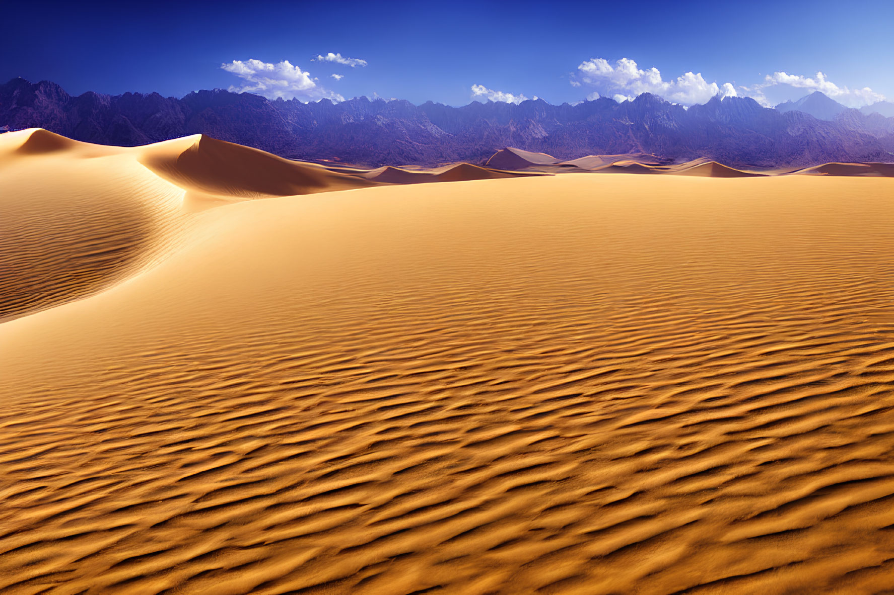Ripple-patterned golden sand dunes and rugged mountains under a blue sky