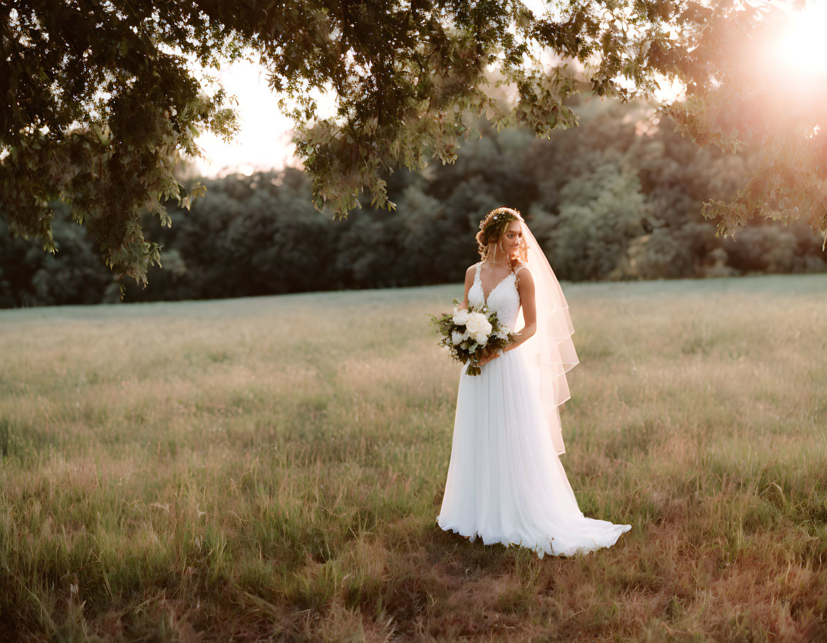 Bride in white dress with bouquet in sunny field