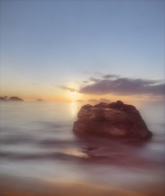 Tranquil sunset seascape with large rock and misty water