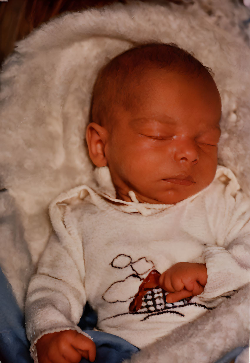 Newborn baby sleeping in white swaddle blanket with teddy bear onesie