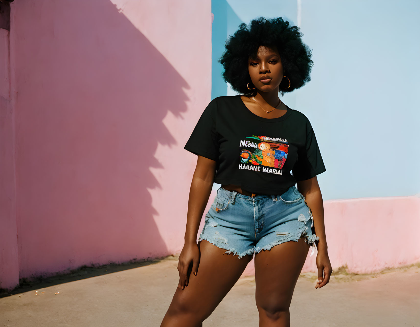 Woman with Afro Hair in Black T-shirt and Denim Shorts Against Pink Wall