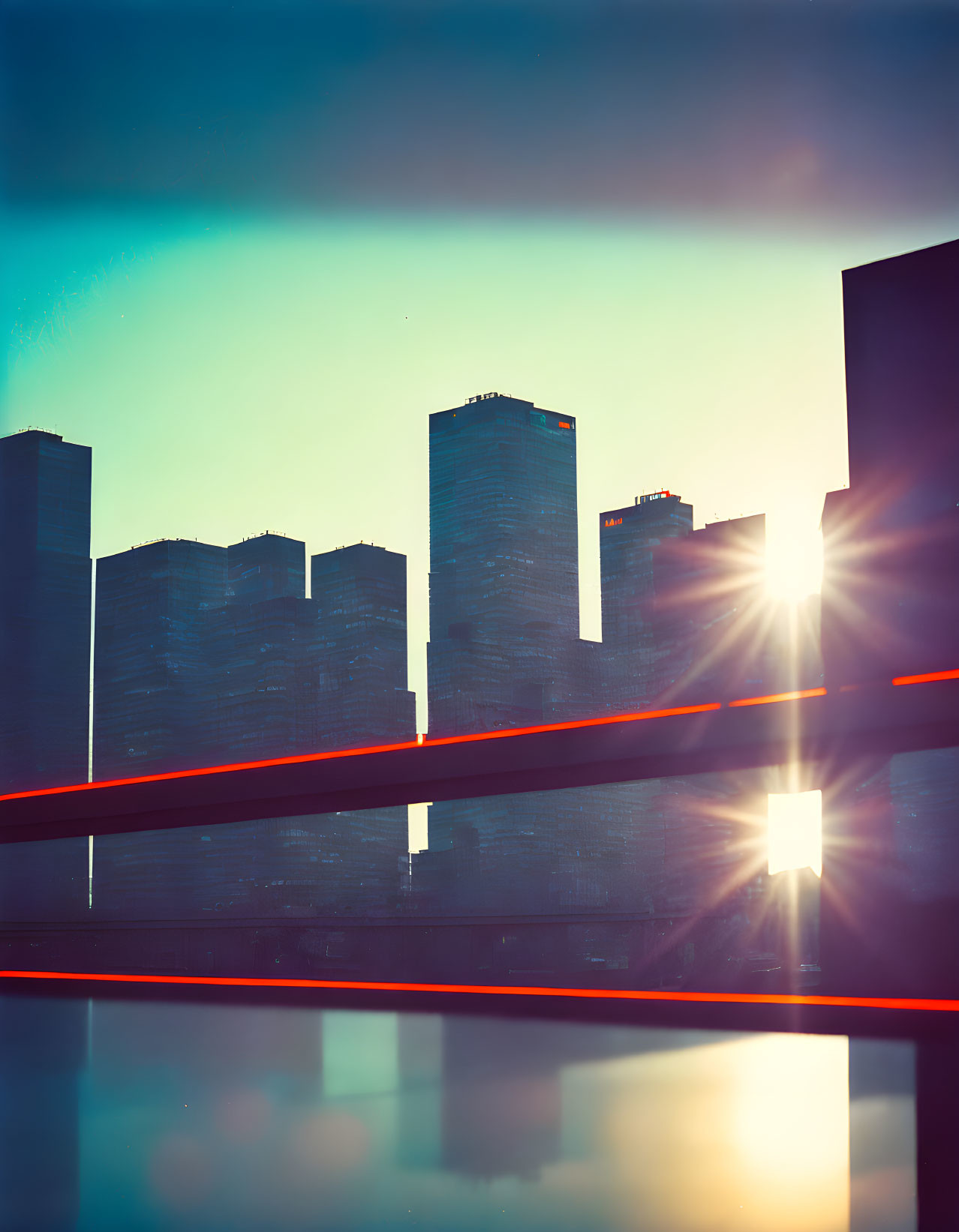 Urban sunset with skyscrapers, lens flare, light trails, and glossy surface reflection.