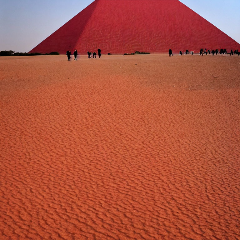 People walking near a large red sand dune under a clear blue sky