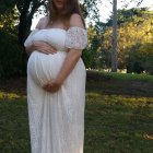 Pregnant woman in white dress with floral crown among wildflowers
