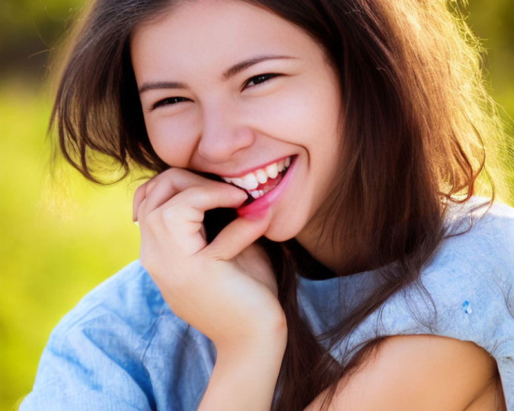 Young woman with long brown hair smiling outdoors with greenery.