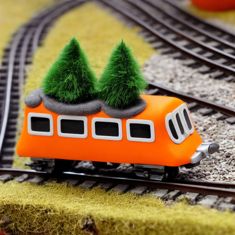Miniature orange toy train with green trees on model tracks and artificial grass
