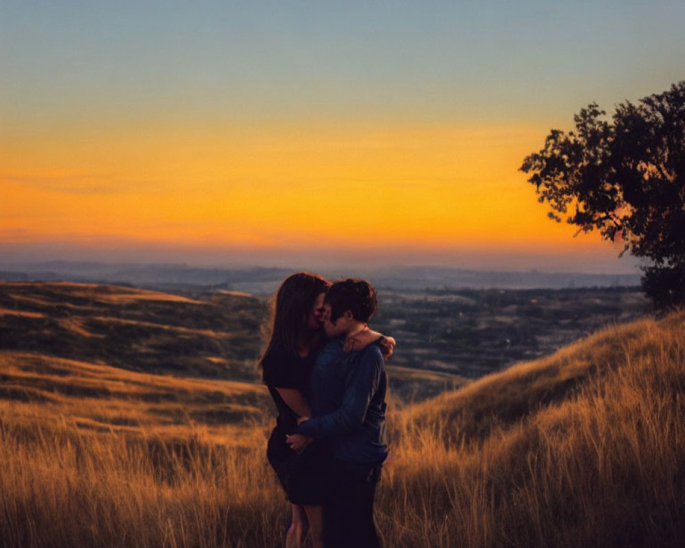 Romantic couple kissing on hill at sunset with golden grass and vibrant sky