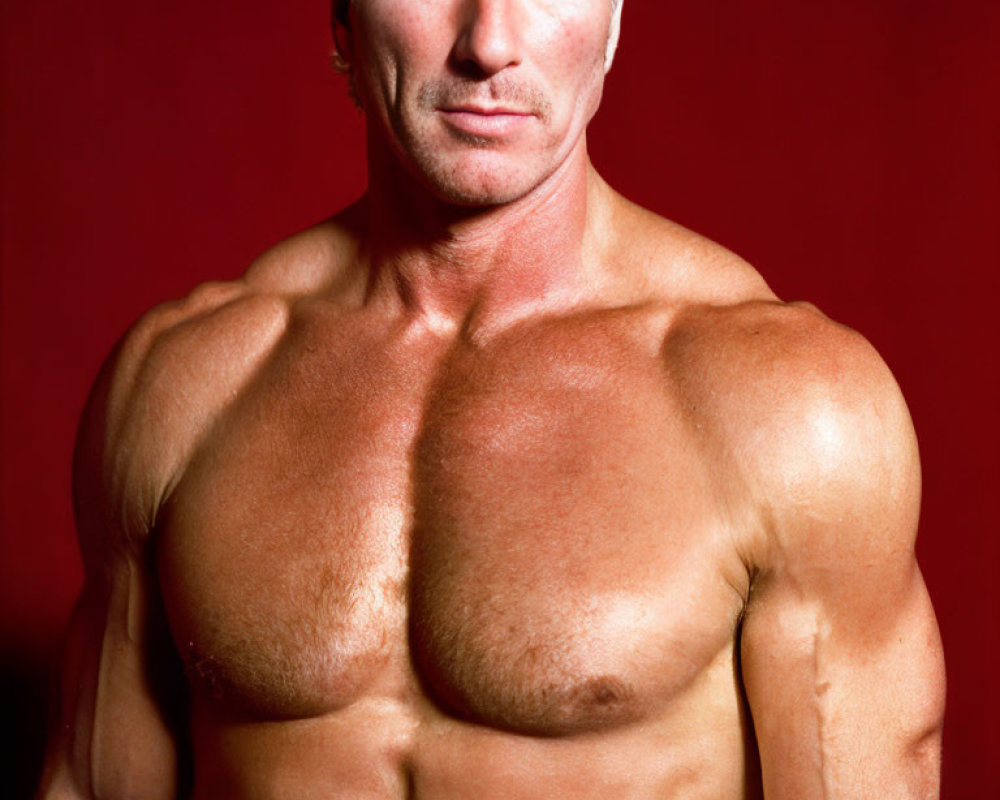 Muscular Man with Blond Hair Poses Against Red Background