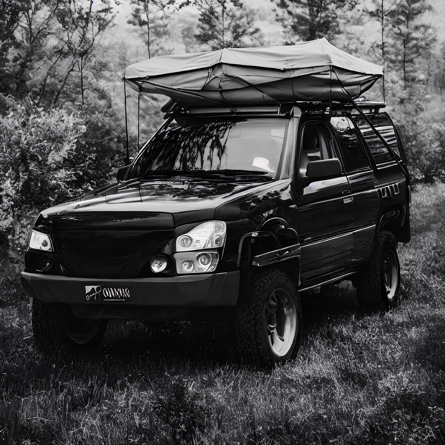 Black off-road vehicle with roof-top tent in forested area for outdoor adventure.