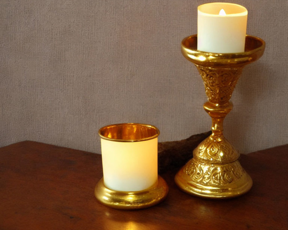 Ornate gold candlestick with lit candle and votive holder on wooden surface
