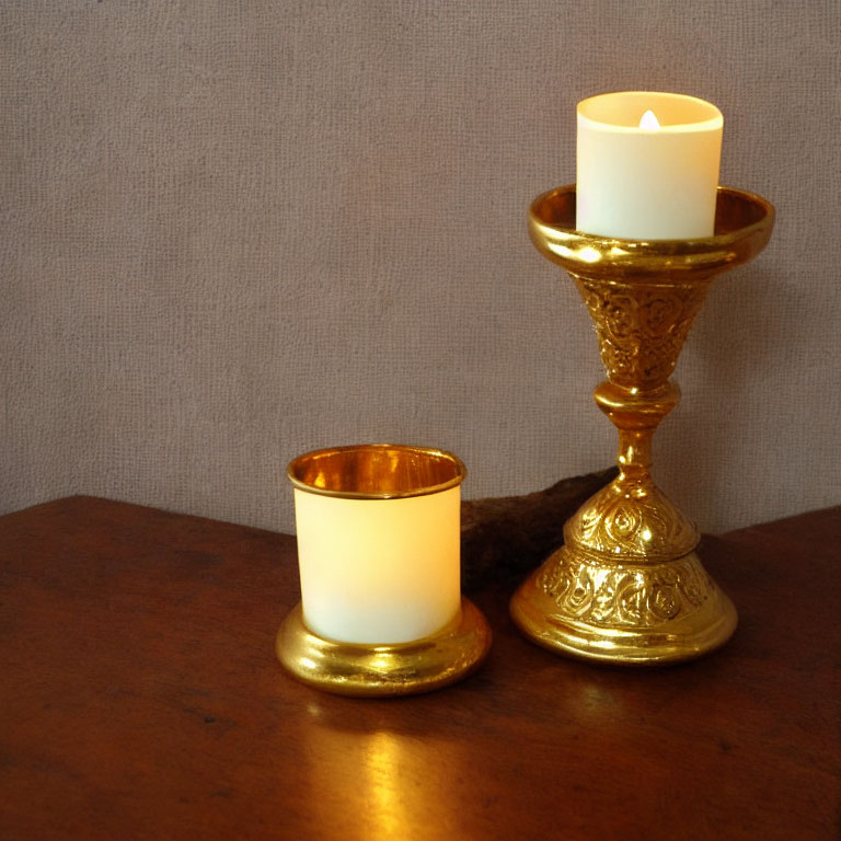 Ornate gold candlestick with lit candle and votive holder on wooden surface