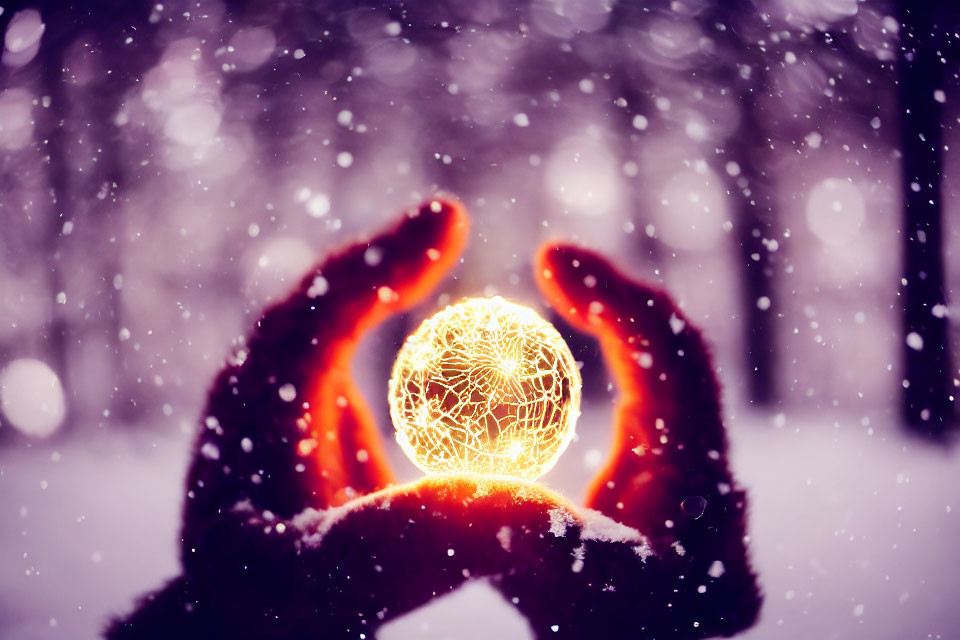 Hands in gloves holding glowing orb in falling snowflakes.