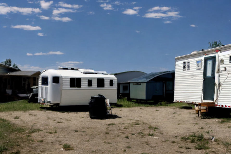 Vintage white trailer and parked vehicles in sunny trailer park.