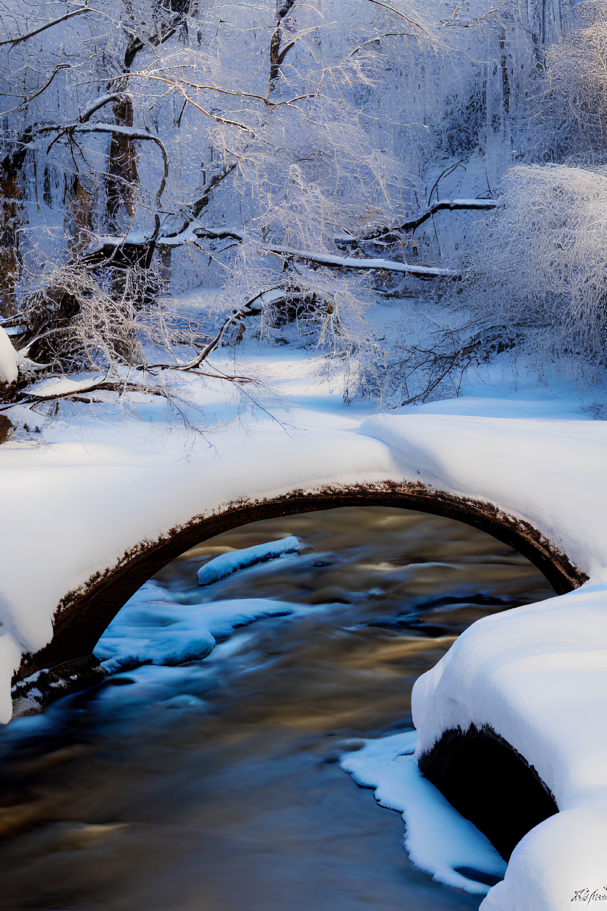Snow-covered stone bridge over flowing creek in serene winter landscape