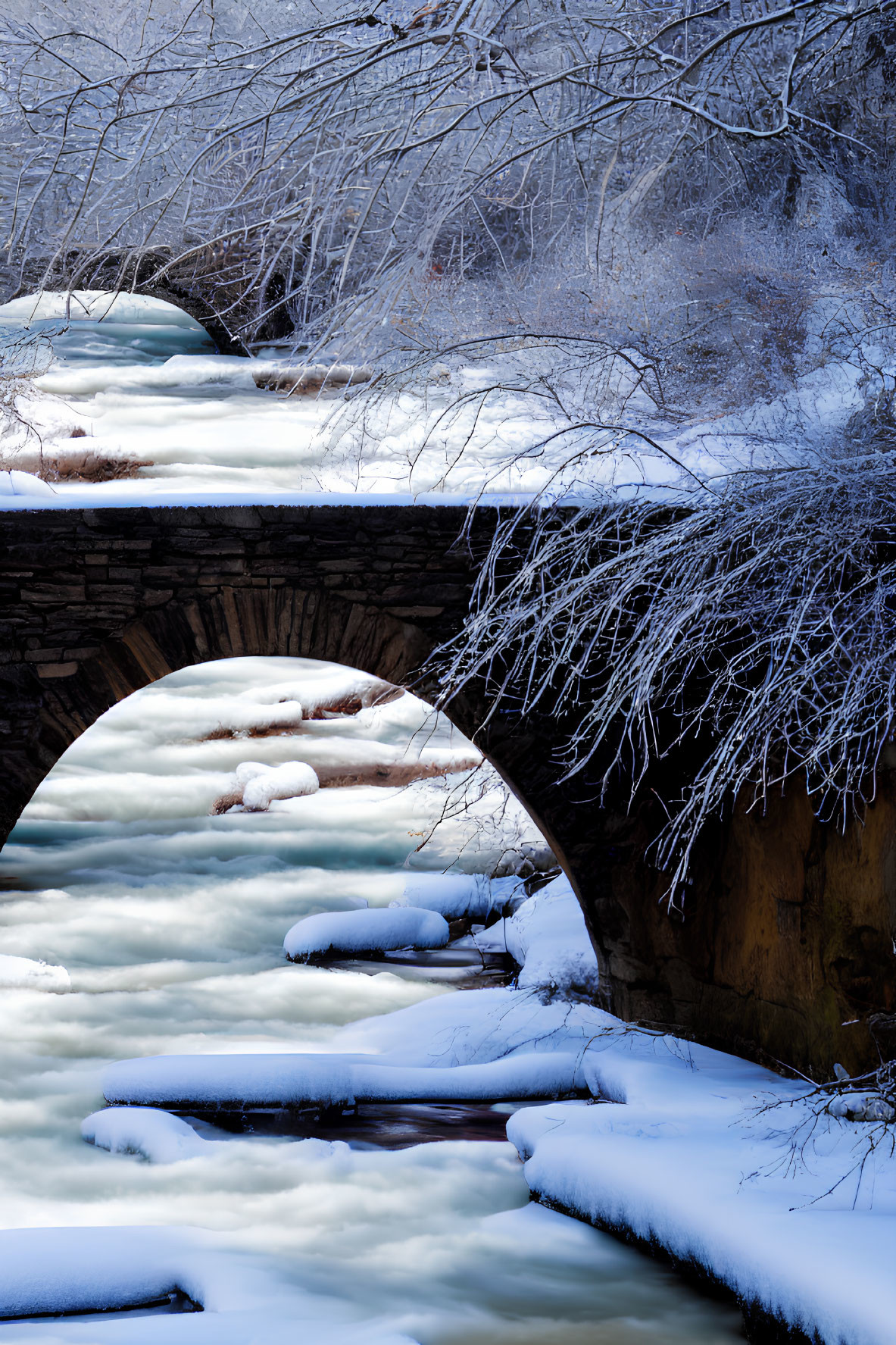 Snow-covered stone bridge over frozen creek in winter landscape