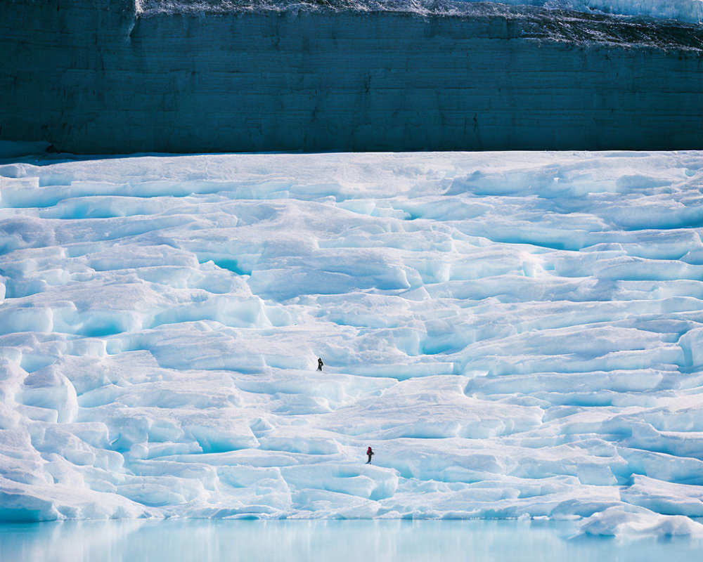 People walking on icy glacier against ice cliff backdrop