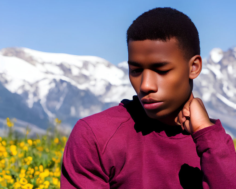 Young man in burgundy hoodie against snowy mountains and wildflowers under blue sky