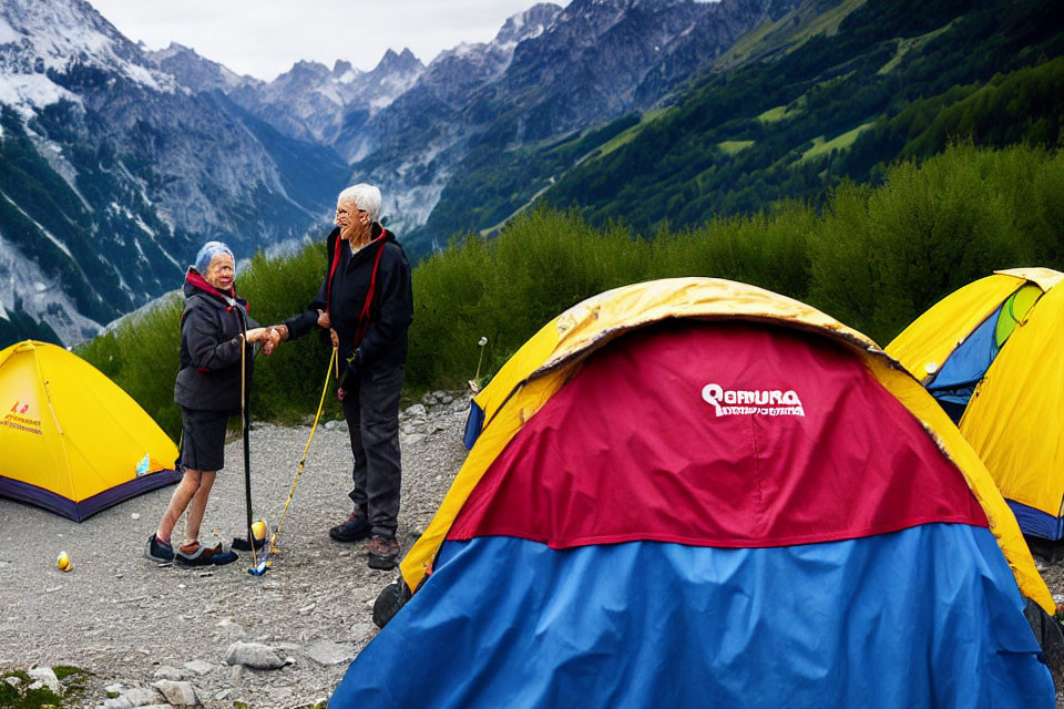 Elderly hikers with walking sticks in front of tents amidst green valleys and mountain peaks