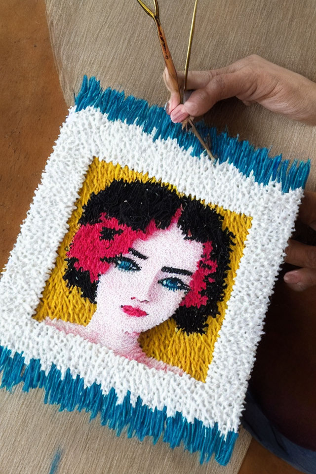 Hand creating latch hook portrait with bright yarns on canvas