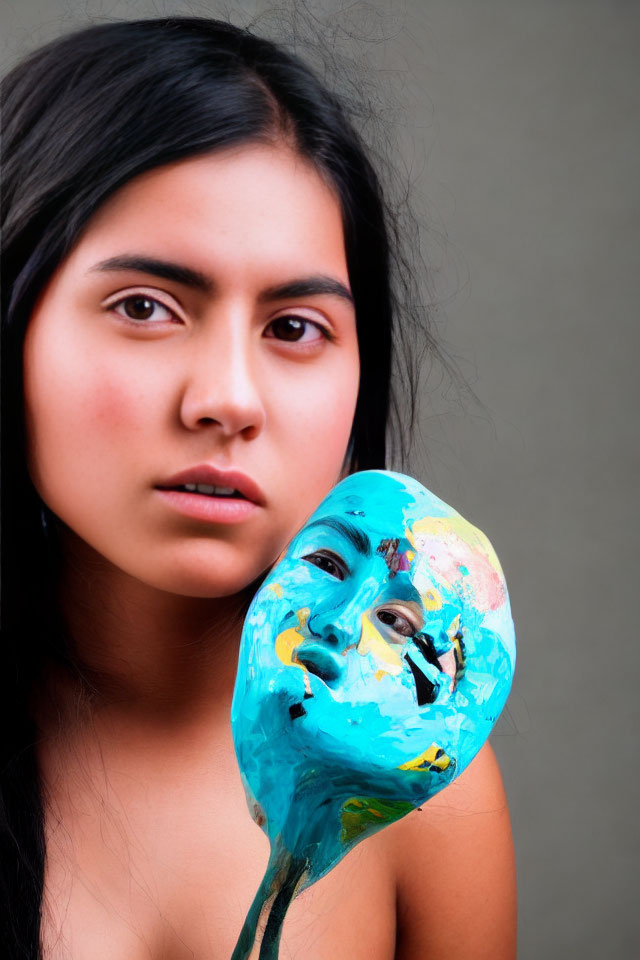 Woman Holding Colorful Painted Mask on Stick with Neutral Background