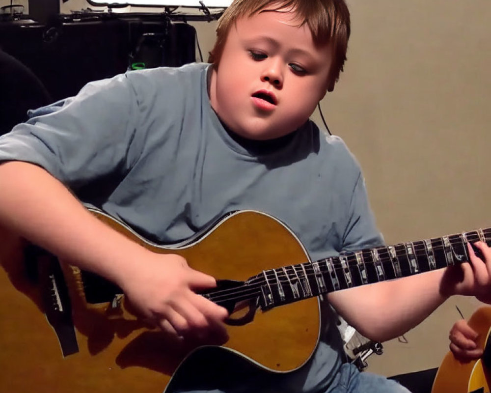 Young boy playing acoustic guitar with musical equipment in background