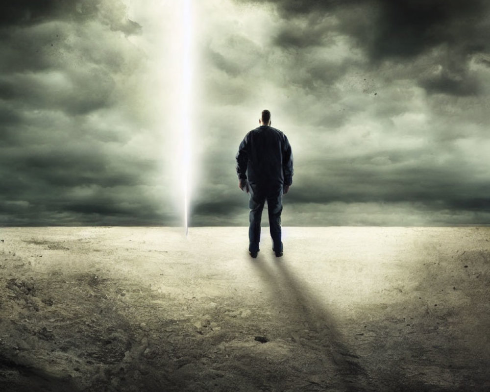 Person standing under dramatic beam of light in desolate landscape