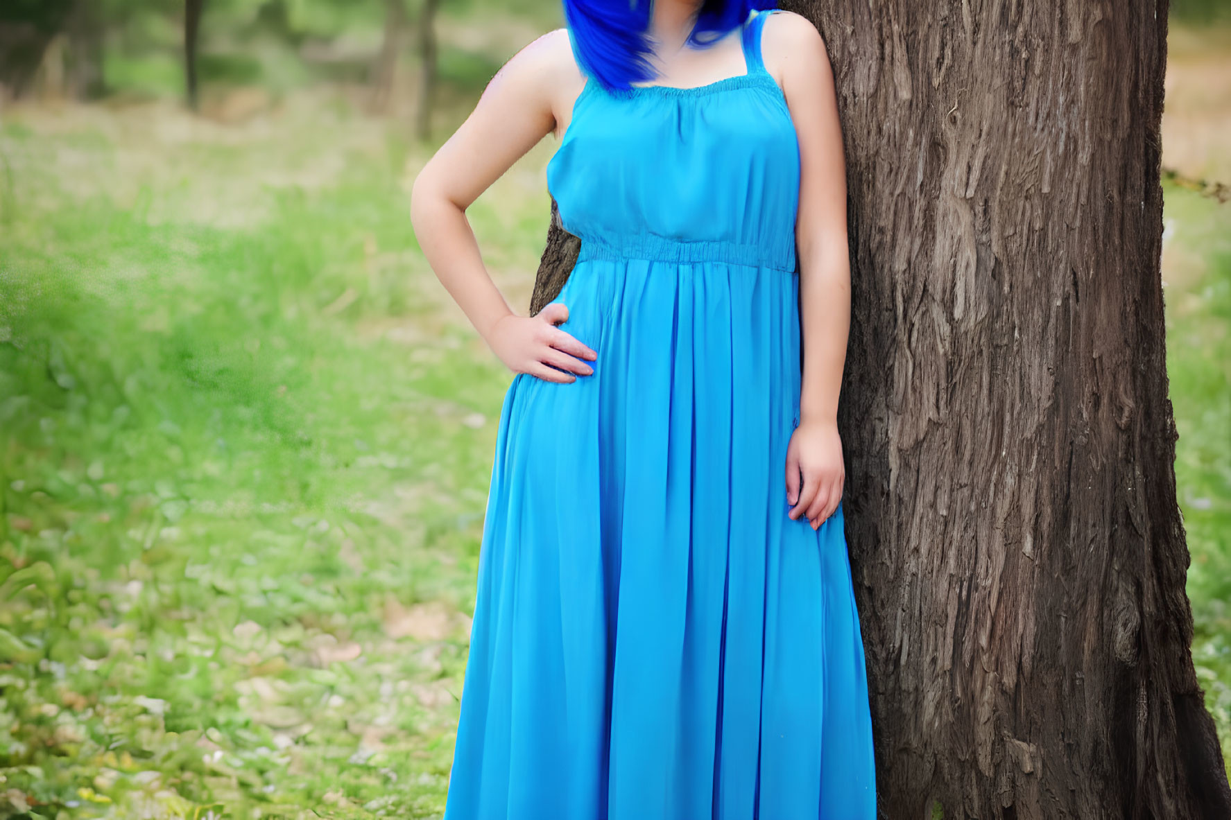 Blue-haired person in long dress by tree in grassy setting