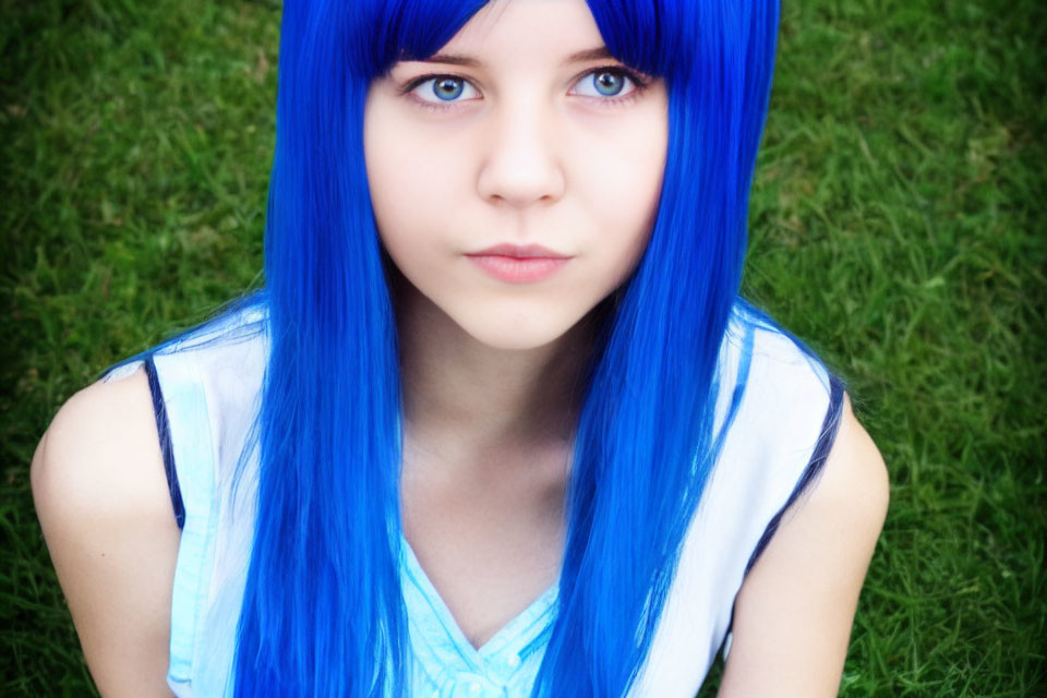 Blue-haired person with blue eyes in front of green grass background